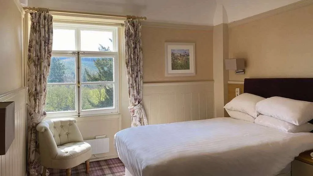 Client bedroom with a double bed, cream armchair and a sash window looking onto trees