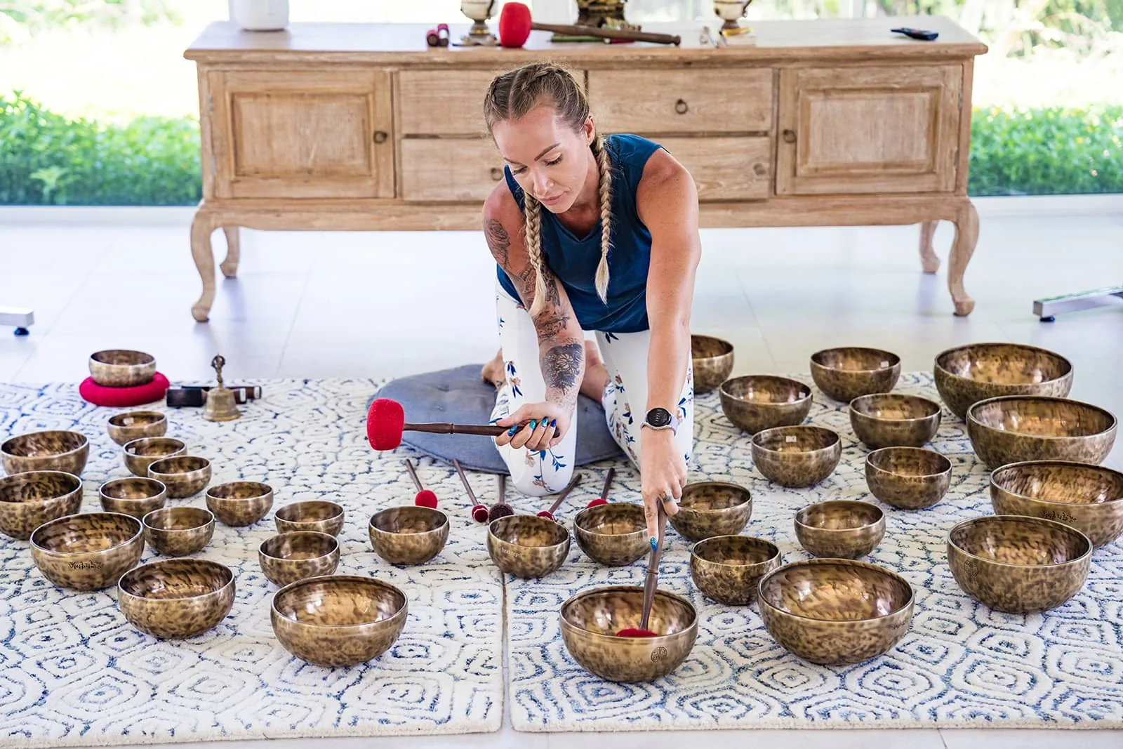 Brass singing bowls of many sizes laid out on patterned mats on a wooden floor in a sound therapy room