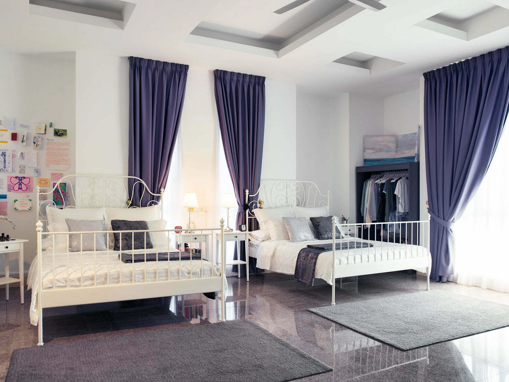 Twin bedroom with two white iron beds, grey rugs, purple curtains and a high coffered ceiling