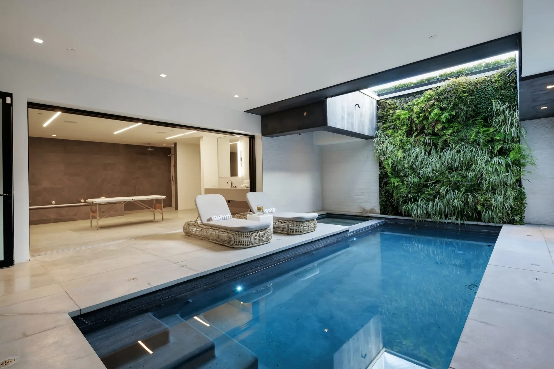 Indoor pool with dark tiles, two loungers and a planted living wall under a skylight