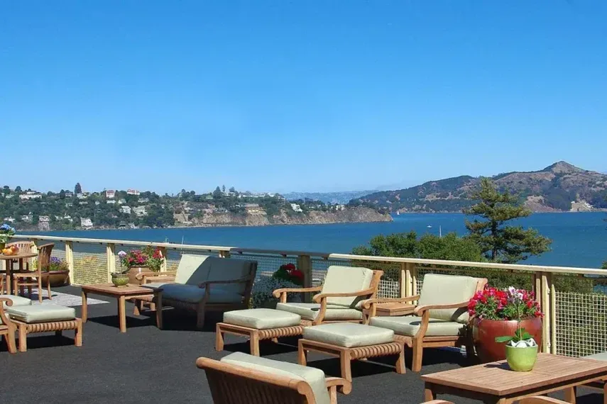 Deck with cushioned lounge chairs and potted flowers above the bay and distant green hills