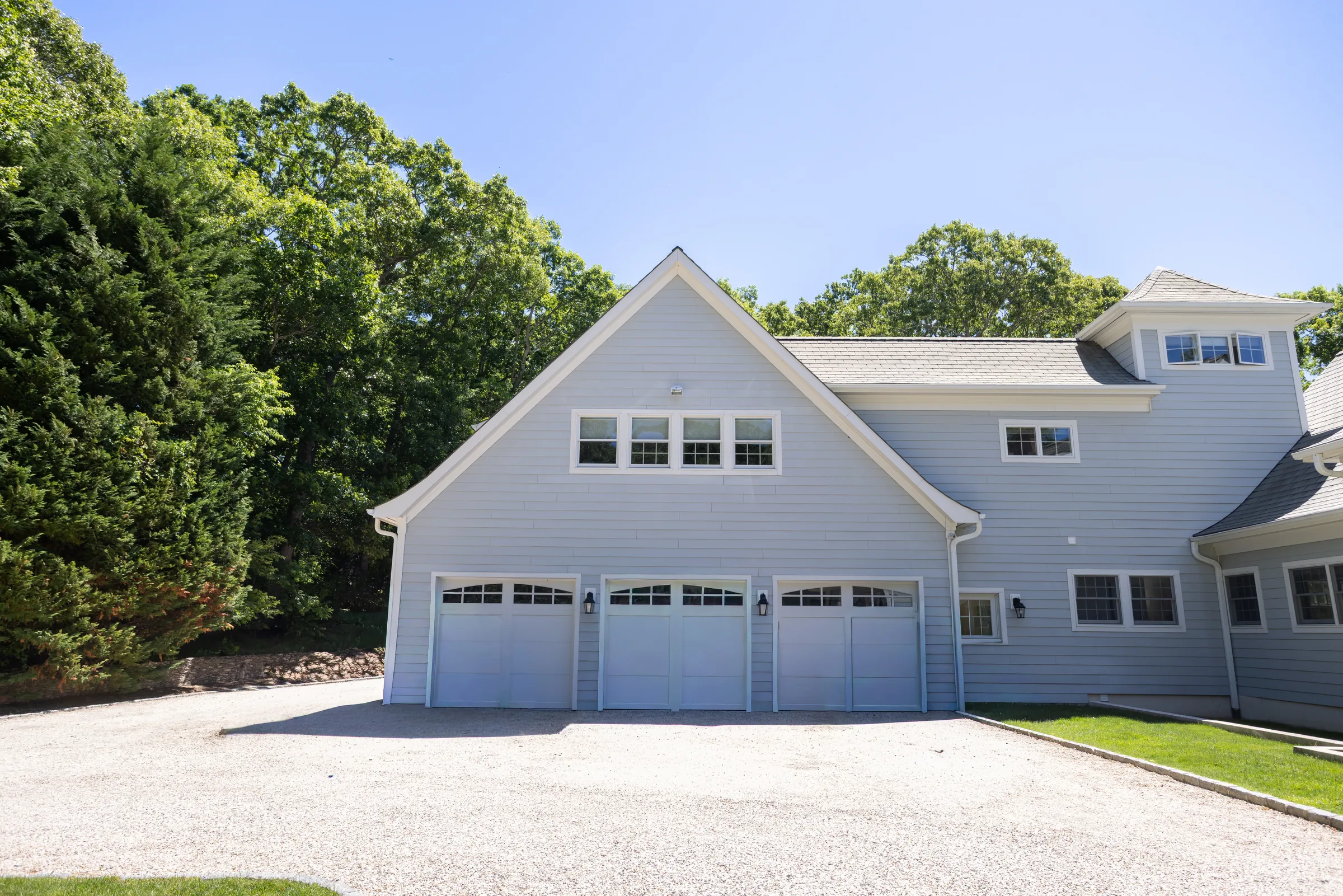 Stone terrace with a stainless steel outdoor kitchen, glass dining table and lawn beyond