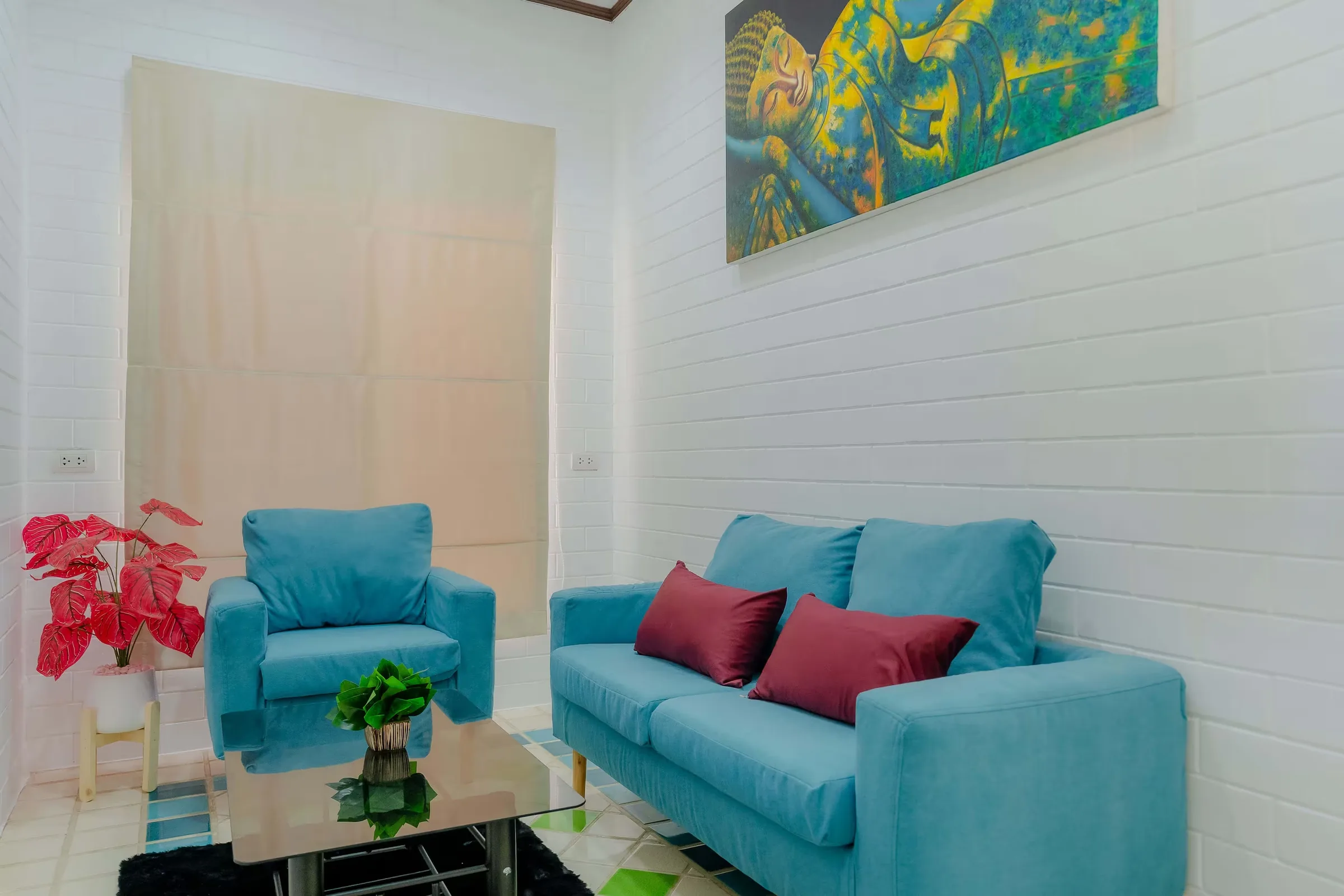 Therapy room with turquoise armchair and sofa, red cushions, a glass coffee table and abstract painting