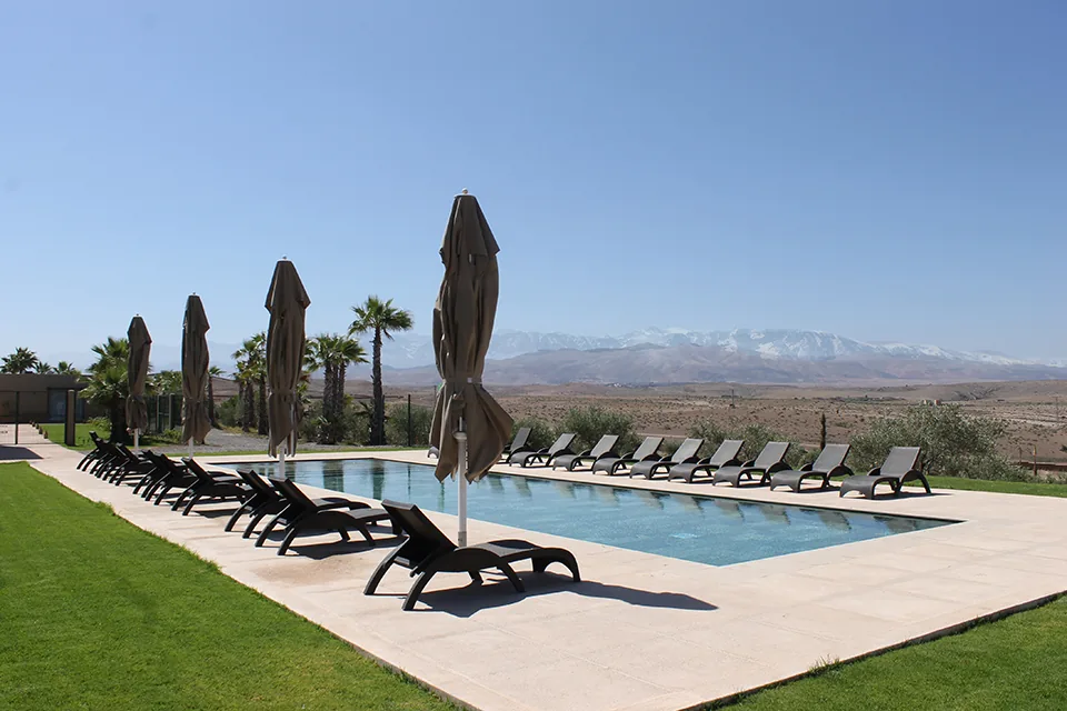 Outdoor pool with sun loungers and parasols on a lawn, snow-capped mountains on the horizon