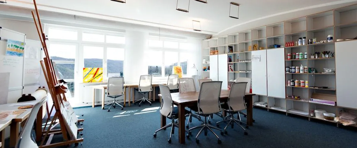 Bright creative room with an easel, a long work table, office chairs and shelves of art supplies
