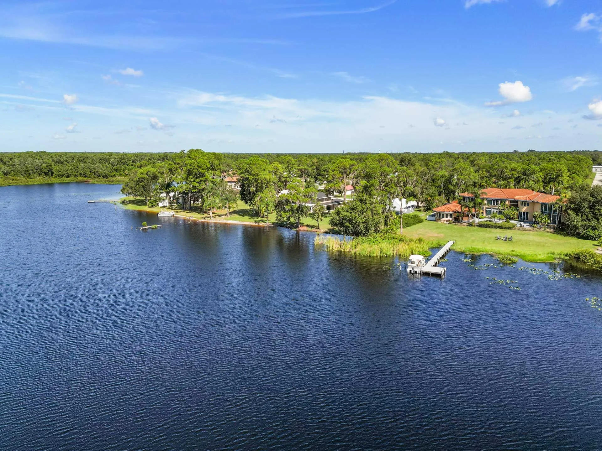 Aerial view across a dark blue lake to the house, lawn and private dock on the wooded shoreline