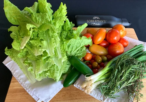 Fresh lettuce, tomatoes, cucumbers, spring onions and herbs laid out on a wooden board