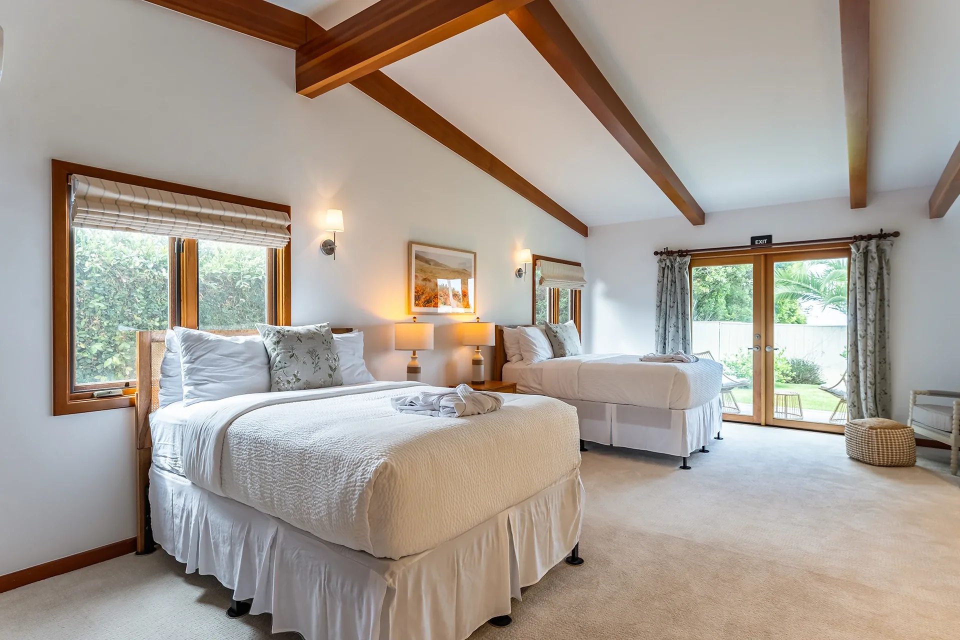 Bright bedroom with two made beds, a beamed ceiling and glass doors opening to the garden