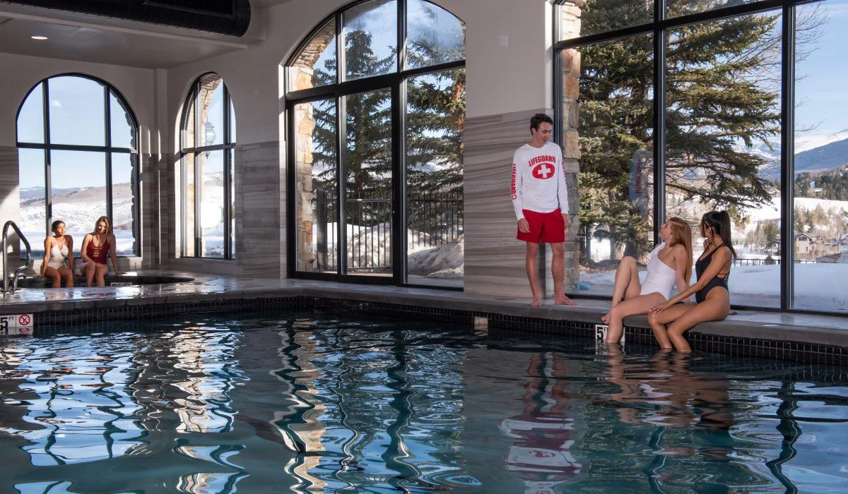 Indoor swimming pool with tall arched windows looking out on snowy hills and pine trees
