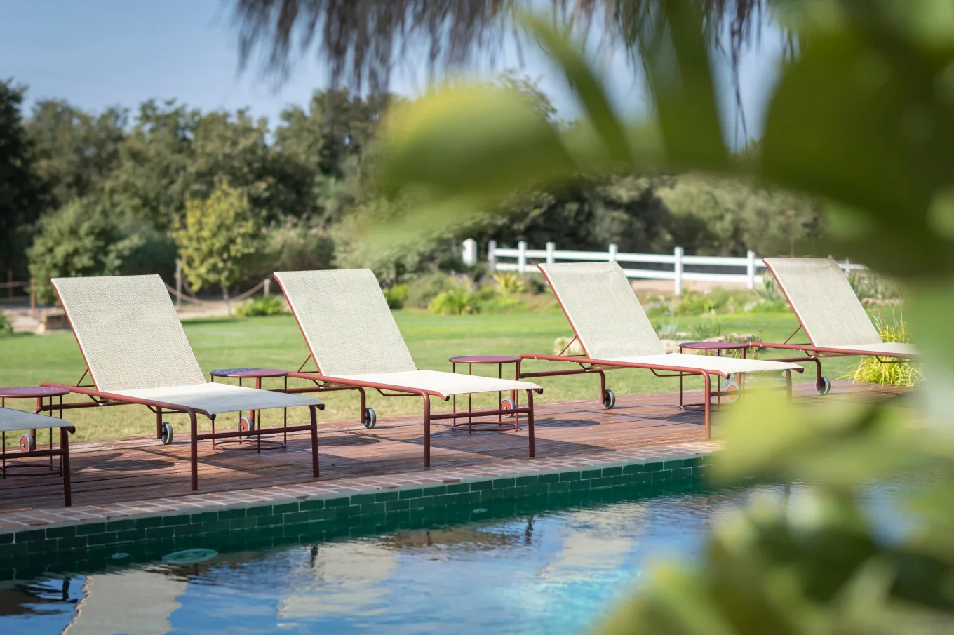 Row of white sun loungers beside a villa swimming pool with lawn and a white fence behind
