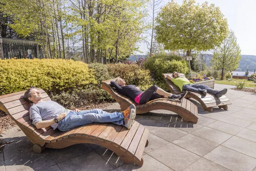 Guests resting on wooden sun loungers on a paved garden terrace surrounded by shrubs and trees