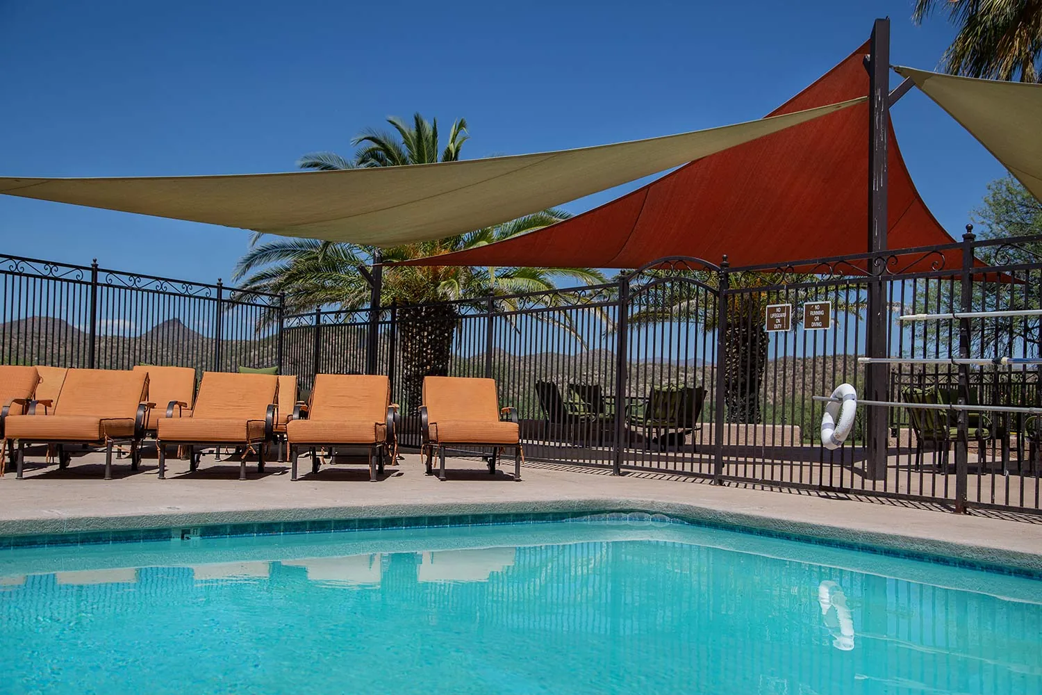 Outdoor pool with orange loungers under red shade sails and desert hills in the distance