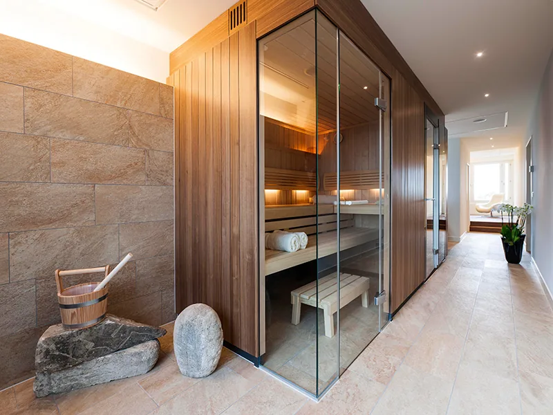 Glass fronted wooden sauna cabin beside a stone wall and a corridor in the spa area