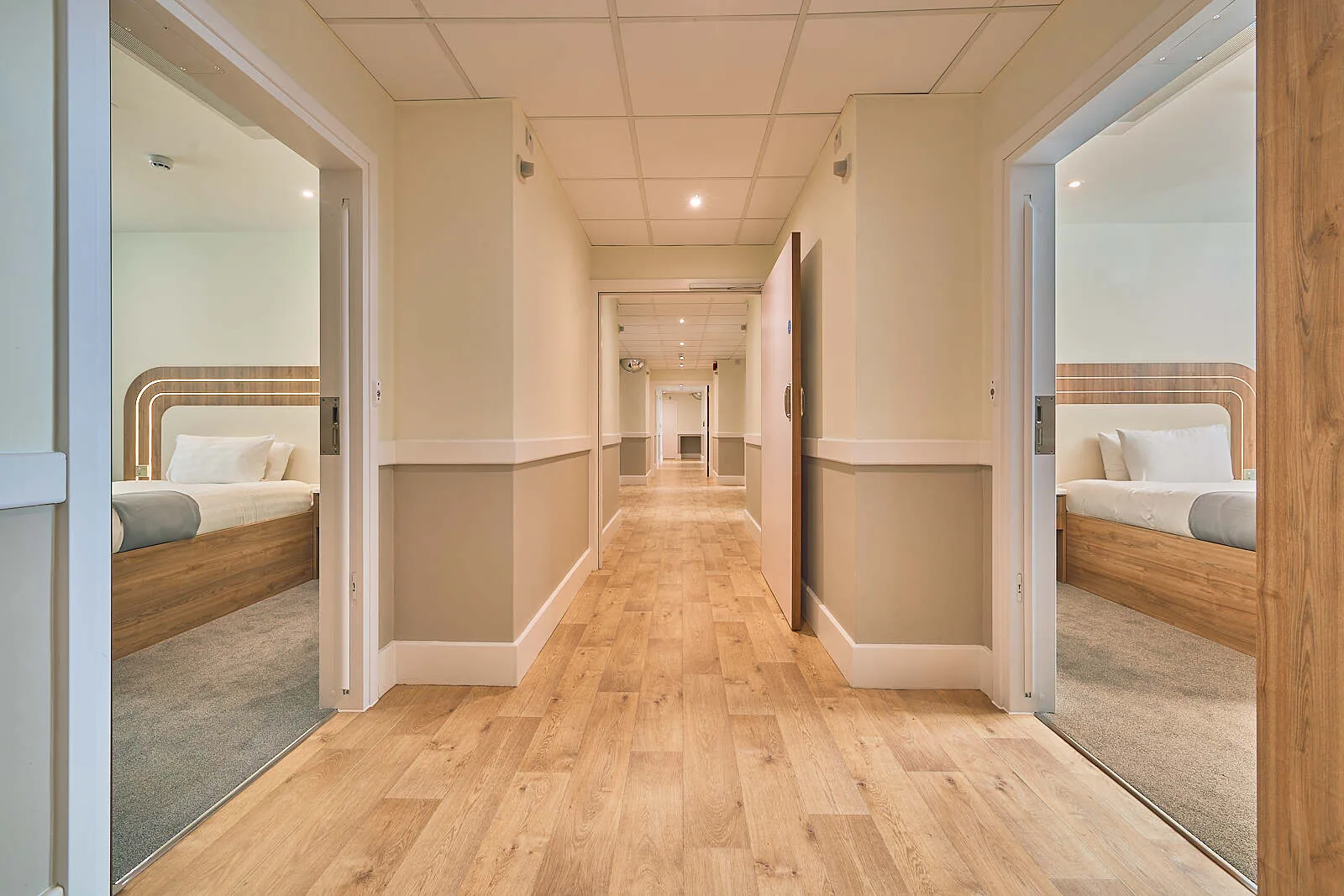 Long ward corridor with wooden flooring and open doors to bedrooms on both sides