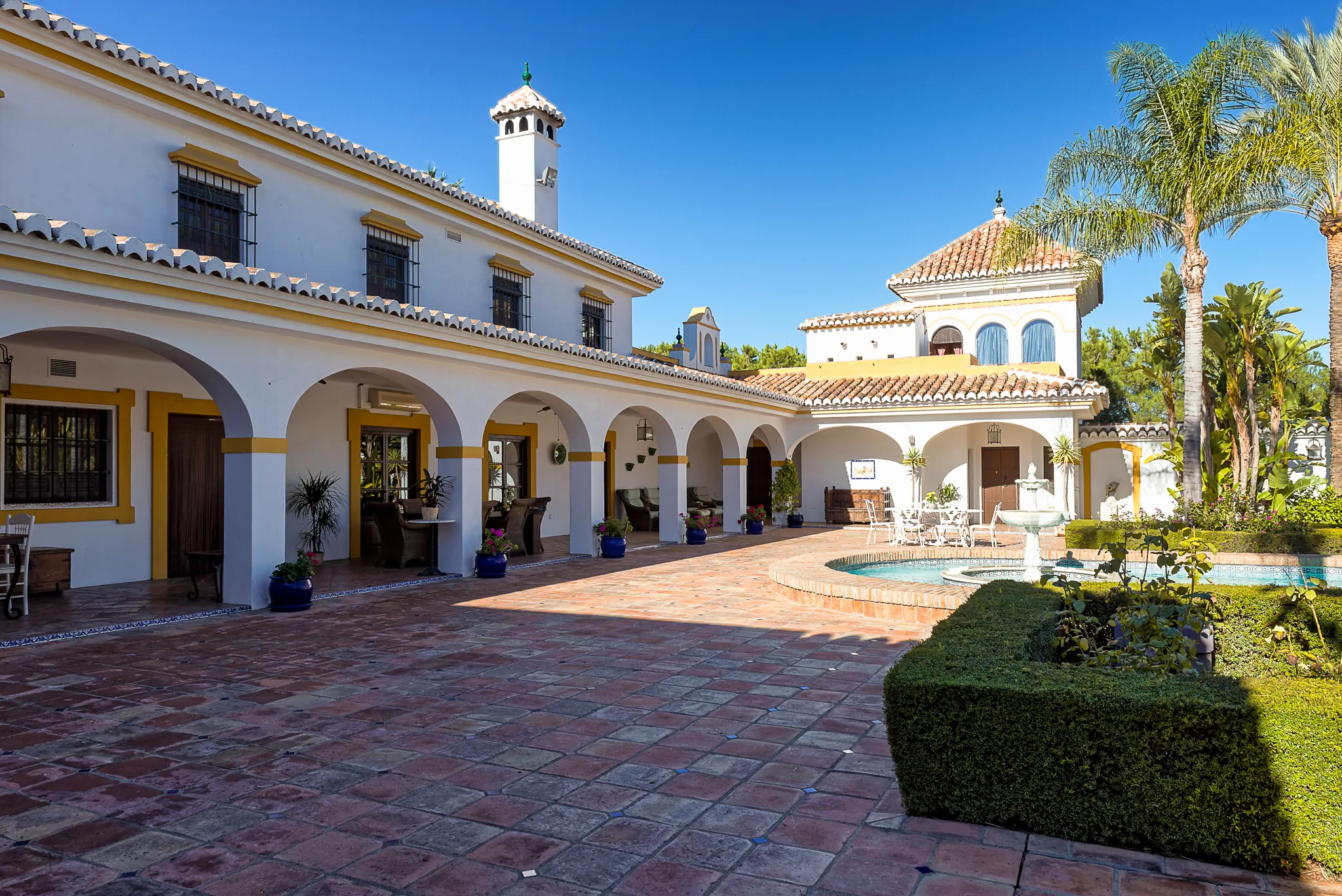White Andalusian main building with arched portico, terracotta courtyard and palms under blue sky