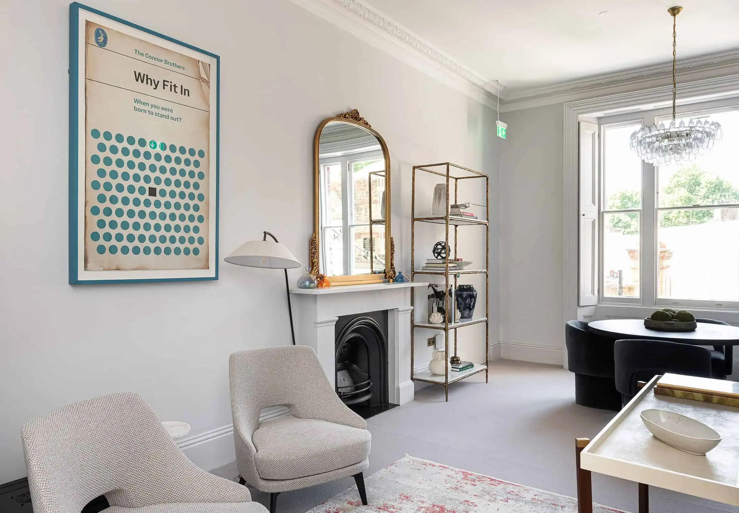 Sitting room with two armchairs, a black fireplace, a gilded mirror and a tall sash window