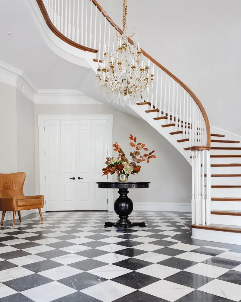 Entrance foyer with a curved white staircase, crystal chandelier and black and white tiled floor