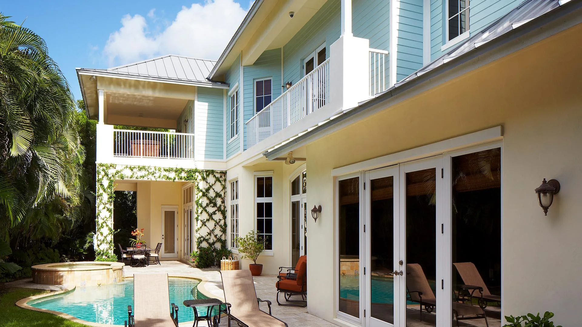 Two storey pale blue residence with balconies, glass doors and a small pool and hot tub in the garden