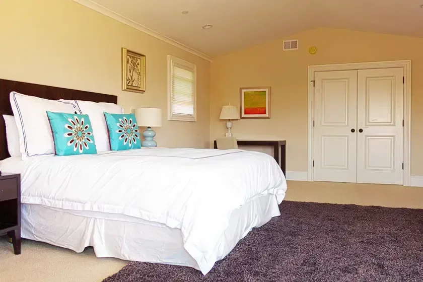 Bedroom with a white double bed, turquoise cushions, dark headboard and a vaulted ceiling