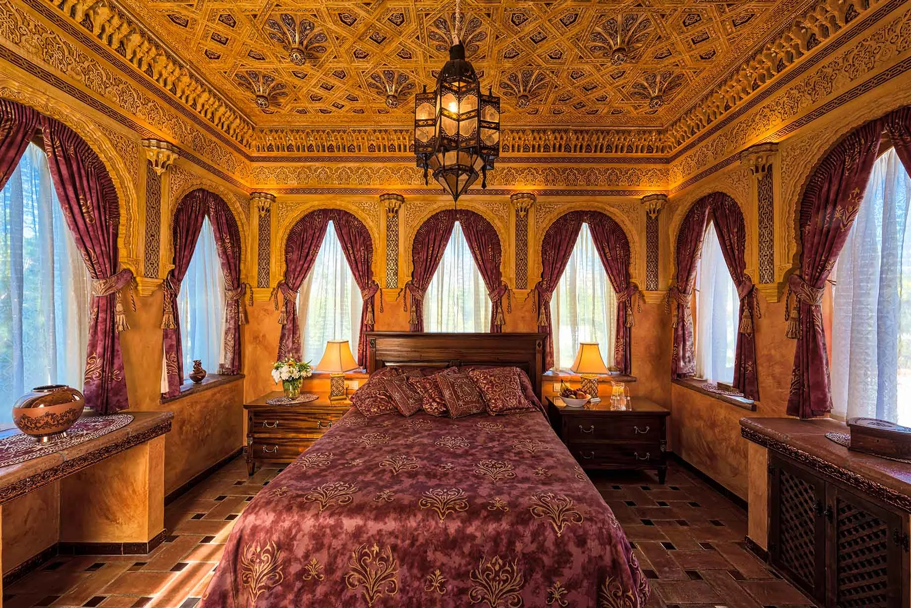 Suite bedroom in Moorish style with carved gilded ceiling, arched windows, red drapes and a lantern