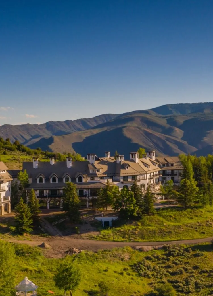 Summer aerial view of the lodge on a green hillside with forested mountain ridges behind