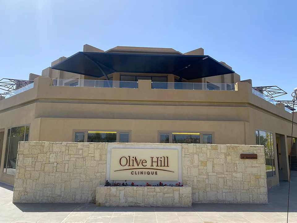 Beige clinic building with a stone wall bearing the Olive Hill Clinique name sign