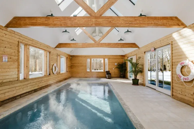 Indoor lap pool in a wood-panelled pool house with exposed timber beams and skylights