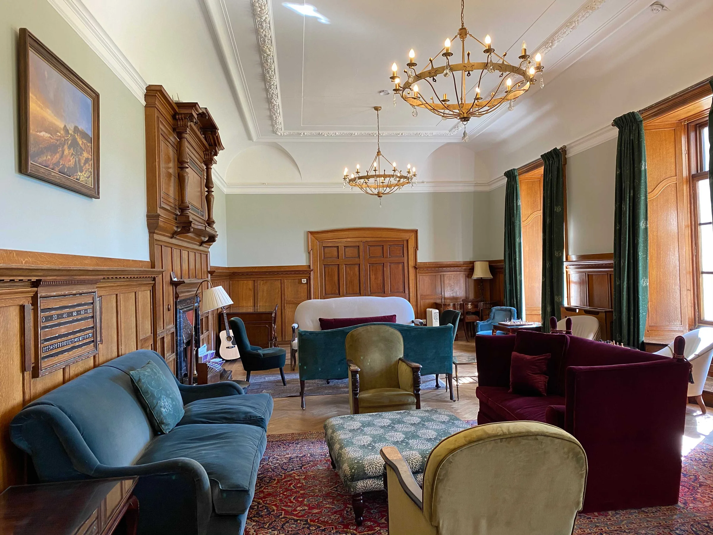 Wood panelled drawing room with crystal chandeliers, green velvet sofas and tall windows