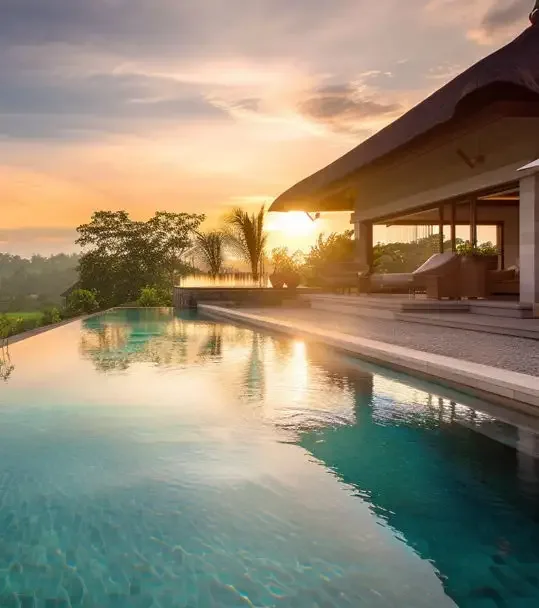 Infinity pool beside a villa terrace with a thatched roof, overlooking palm trees at sunset