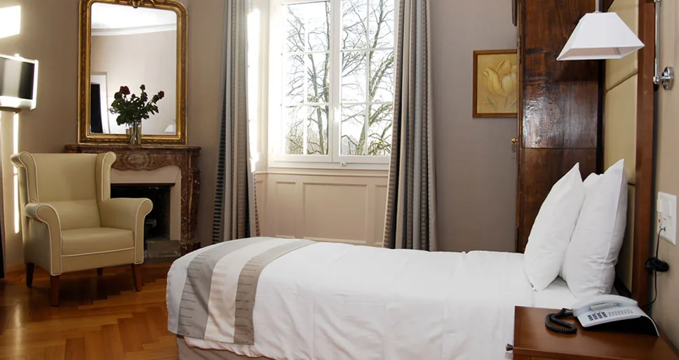 Patient room with a single bed, a wing armchair, a marble fireplace with mirror and a tall window