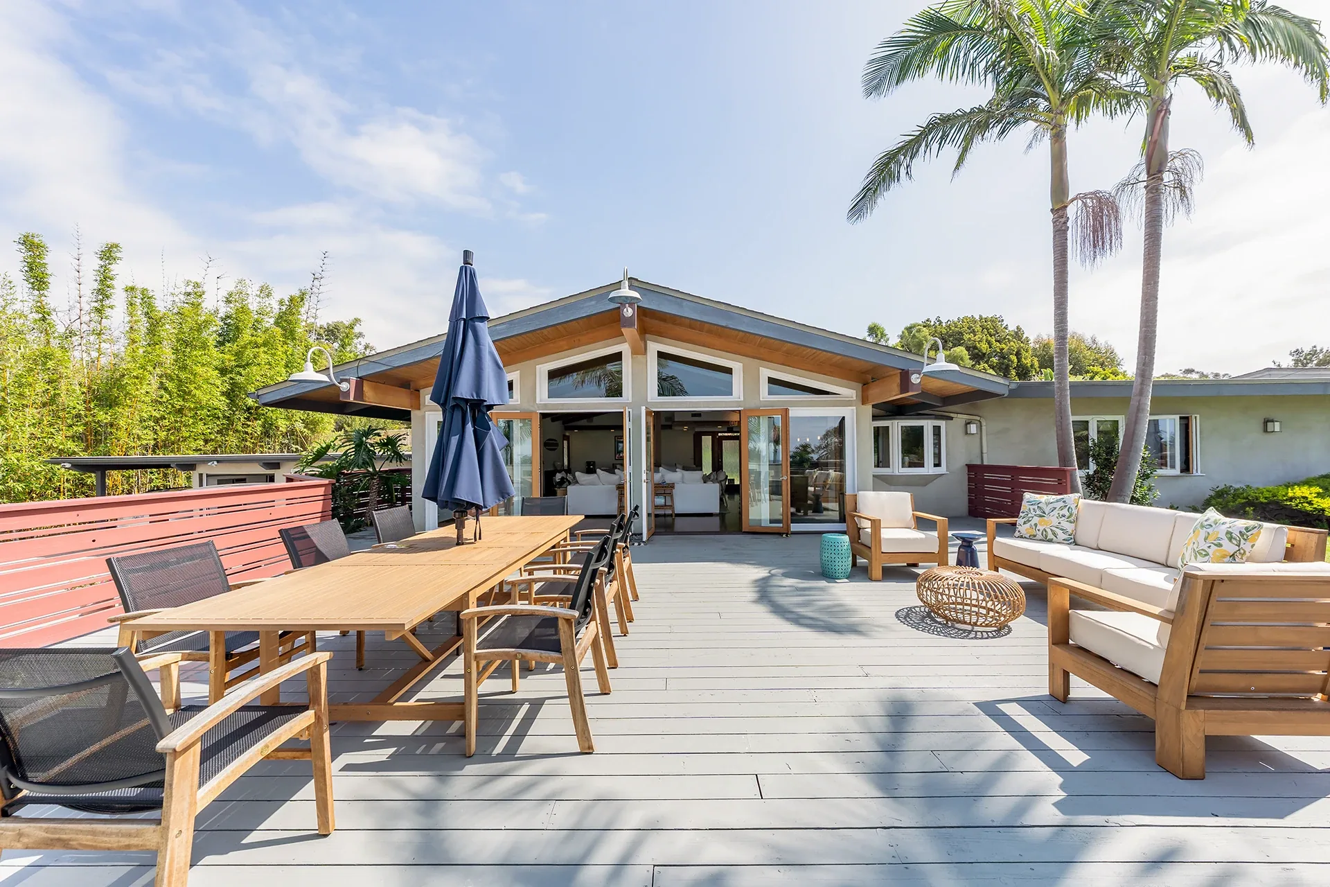 Large wooden deck with a long dining table, lounge chairs and palm trees outside the Point Dume house