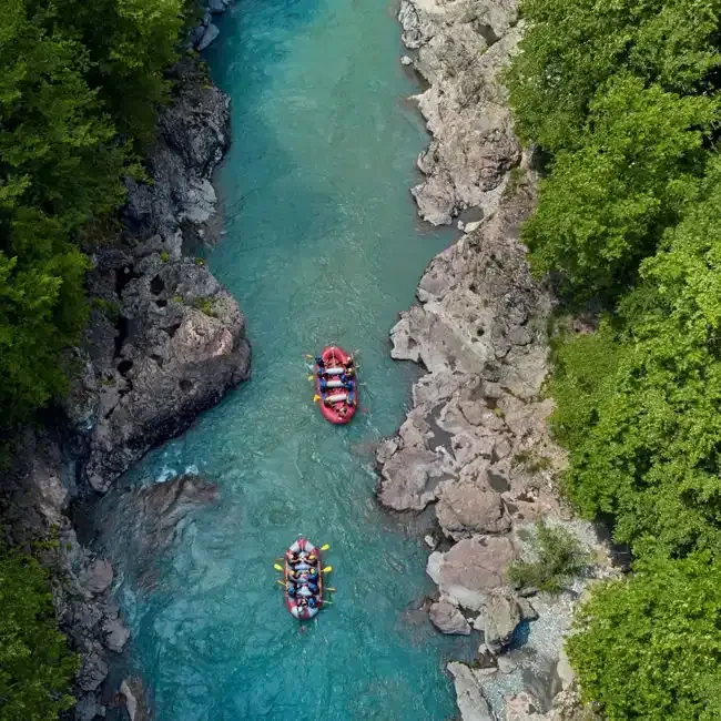 Aerial view of two rafts on a turquoise river running through a rocky, forested gorge