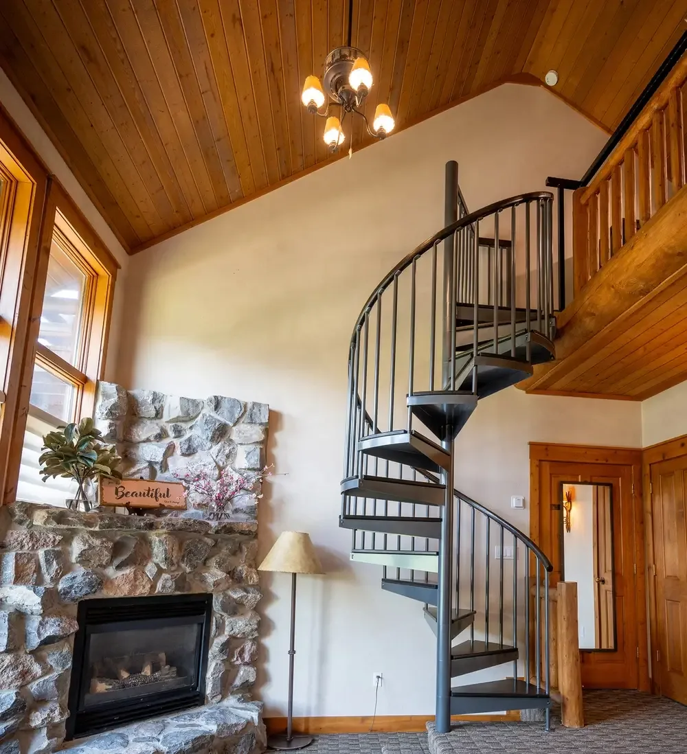 Lodge sitting area with a stone gas fireplace, wood ceiling and a metal spiral staircase