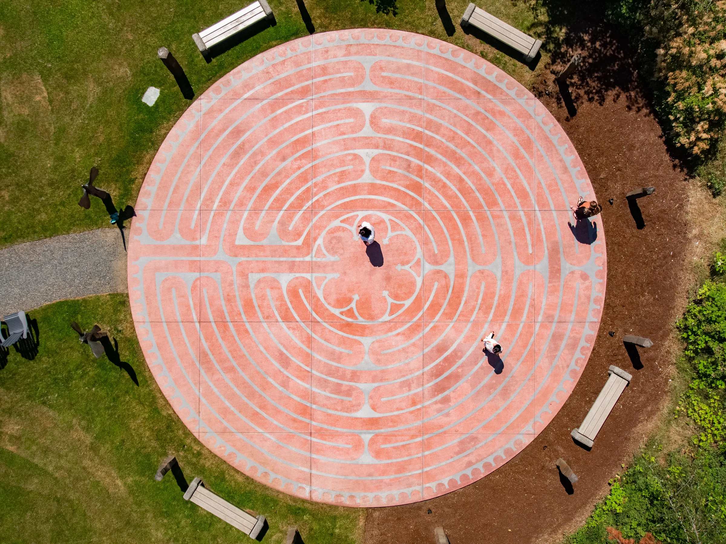 Circular brick walking labyrinth seen from directly above, ringed by benches, mulch and lawn