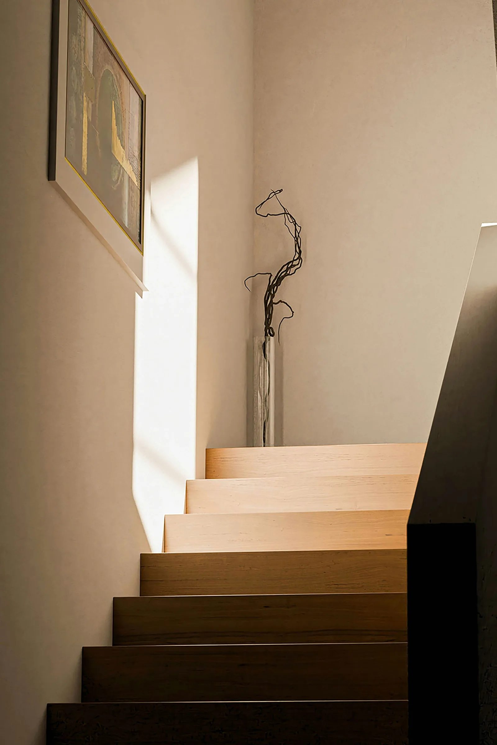 Interior staircase with dark wooden steps lit by daylight, a framed picture and a vase on the landing
