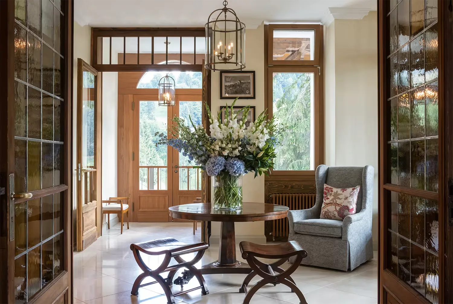 Entrance hall with a round table of flowers, wooden glazed doors and an armchair by the windows