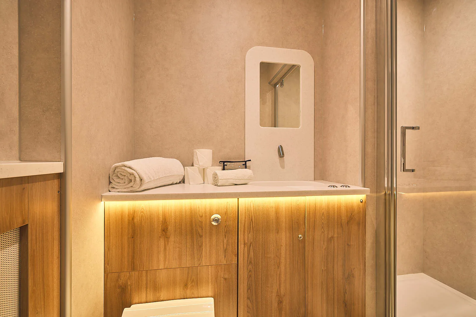 En-suite bathroom with a wood vanity unit, under-lit basin, folded towels and a glass shower door