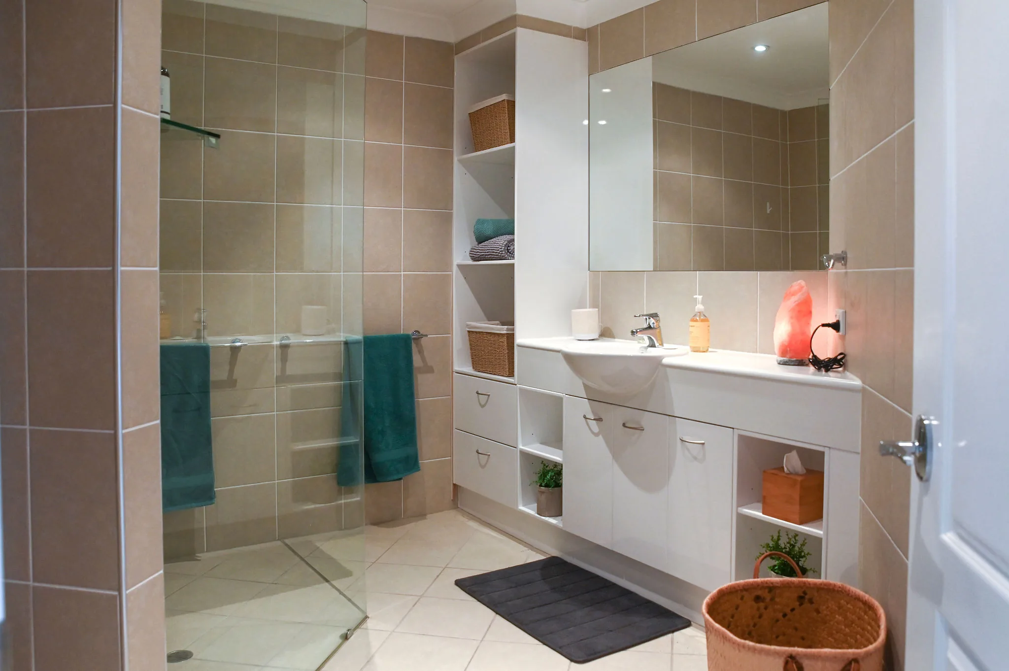 Tiled en-suite bathroom with a walk-in glass shower, white vanity, mirror and green towels