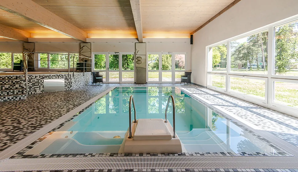 Indoor counter-current swimming pool with mosaic tiles and a wall of windows facing the garden