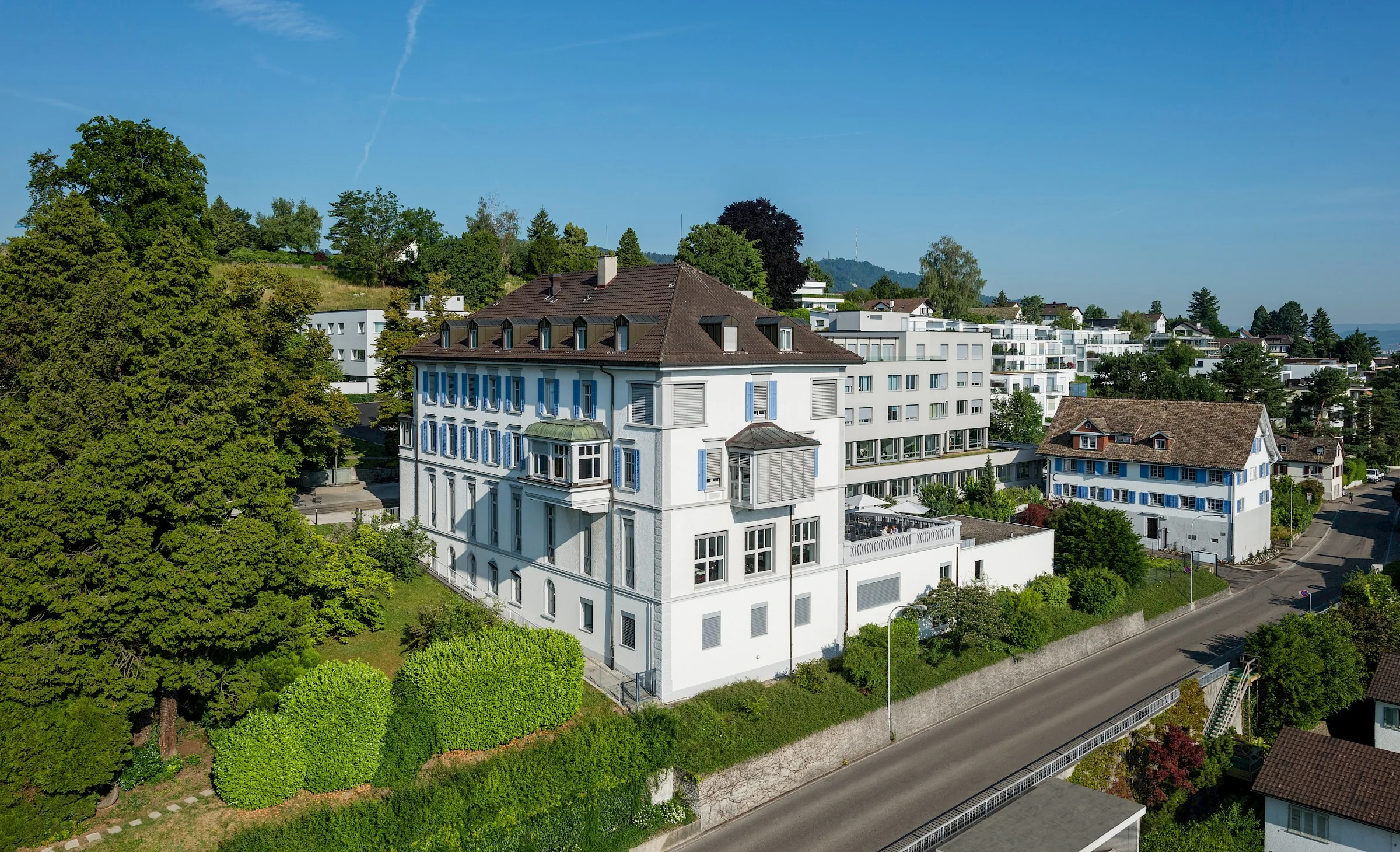 Aerial view of the clinic buildings among trees and hedges beside a road in Kilchberg