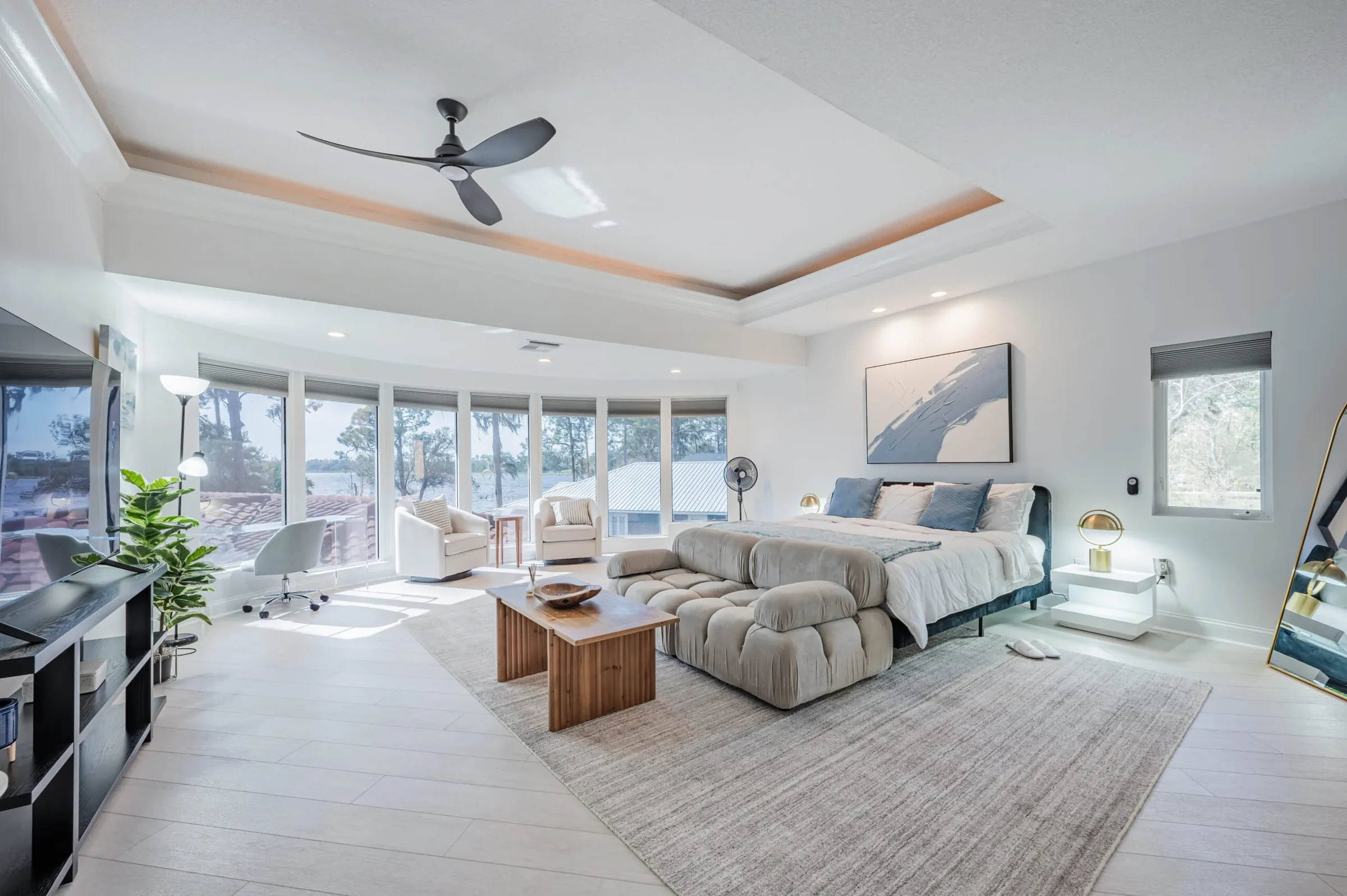 Spacious bedroom suite with a king bed, sofa and coffee table, and a curved wall of windows facing the lake