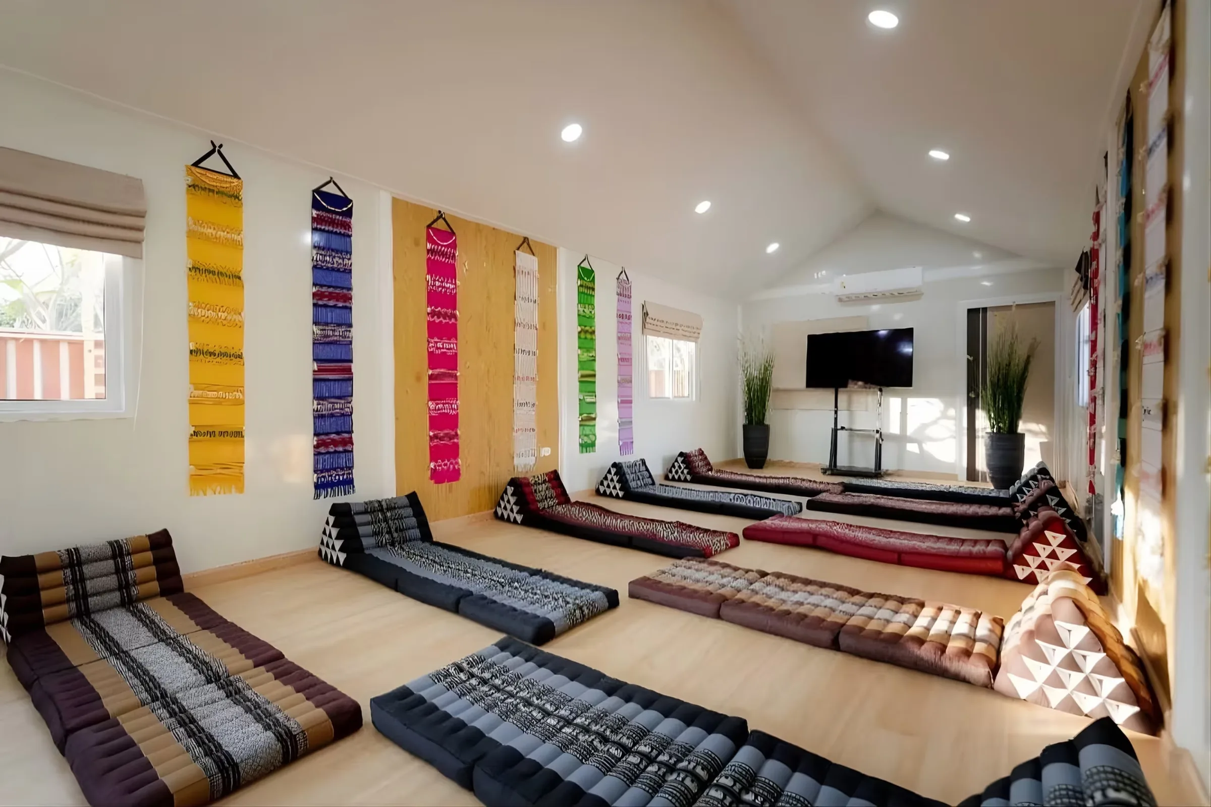 Meditation room with Thai triangle cushions and floor mats in rows under colourful wall hangings