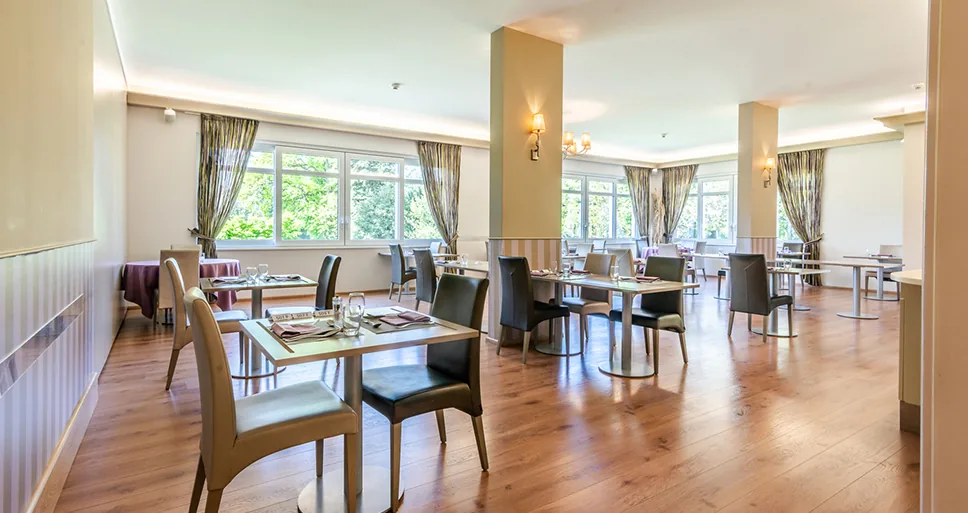 Bright restaurant with laid tables for two, wooden floor, columns and large windows with curtains