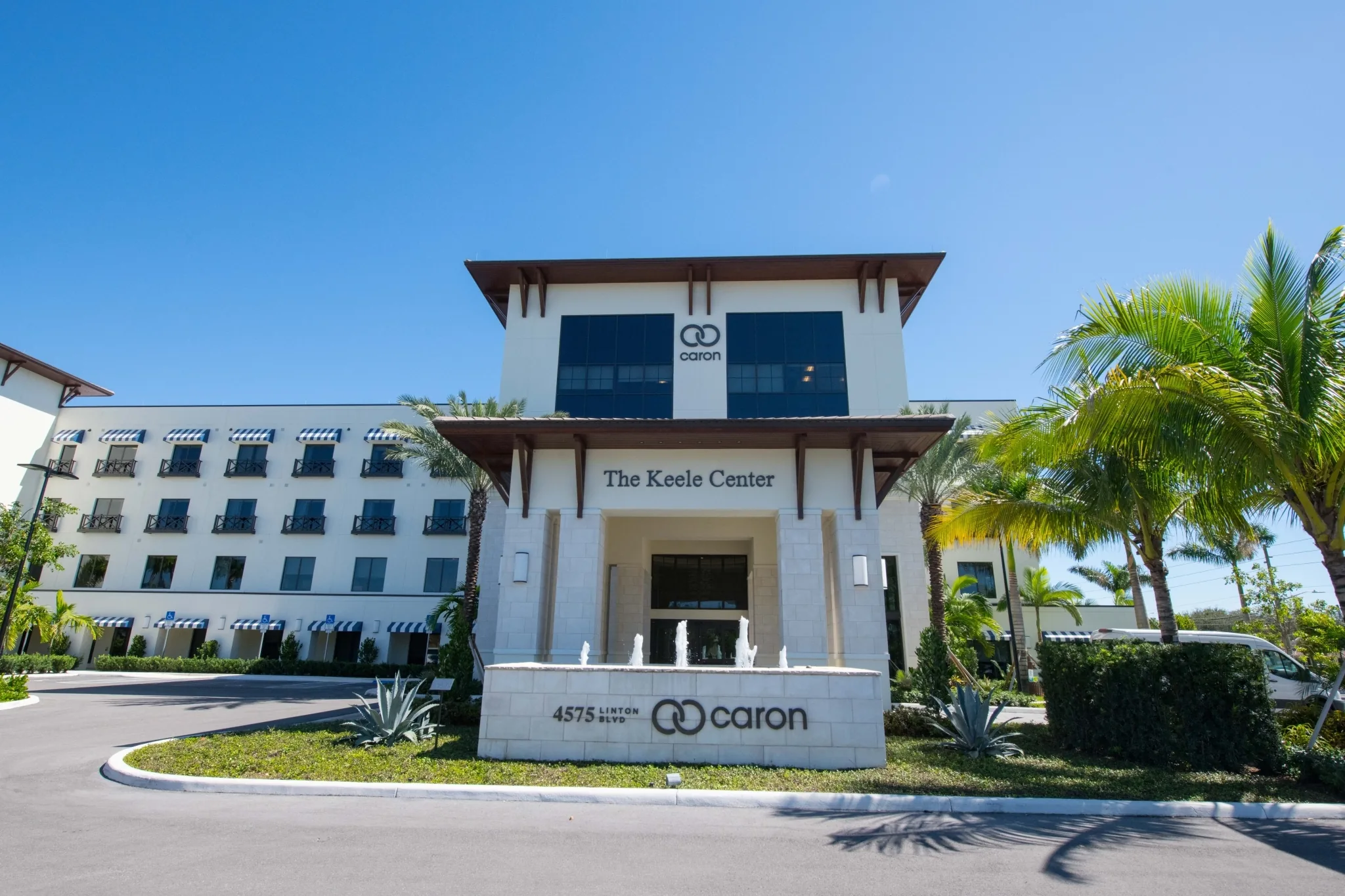 Entrance of The Keele Center, a white multi storey building with palms and a Caron sign at the drive