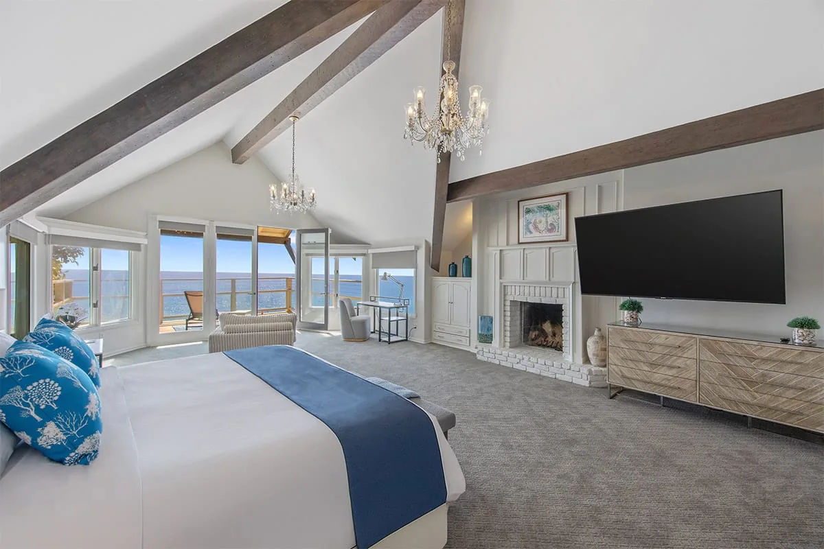 Private suite with a vaulted beamed ceiling, chandelier, fireplace, bed and windows facing the ocean