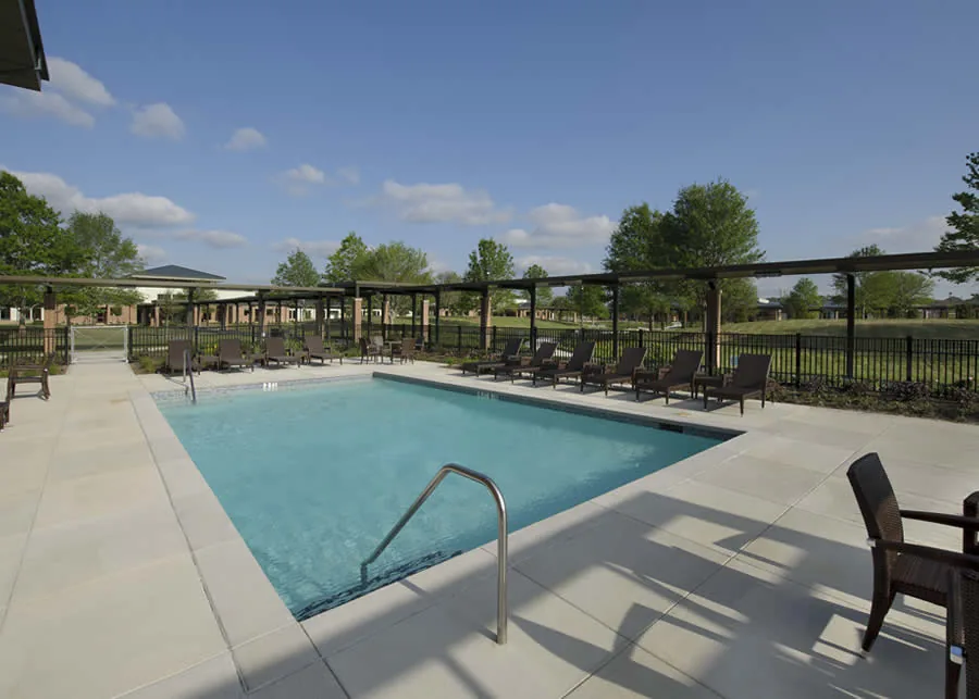 Outdoor saltwater pool with a paved deck, lounge chairs and a fenced lawn under a blue sky