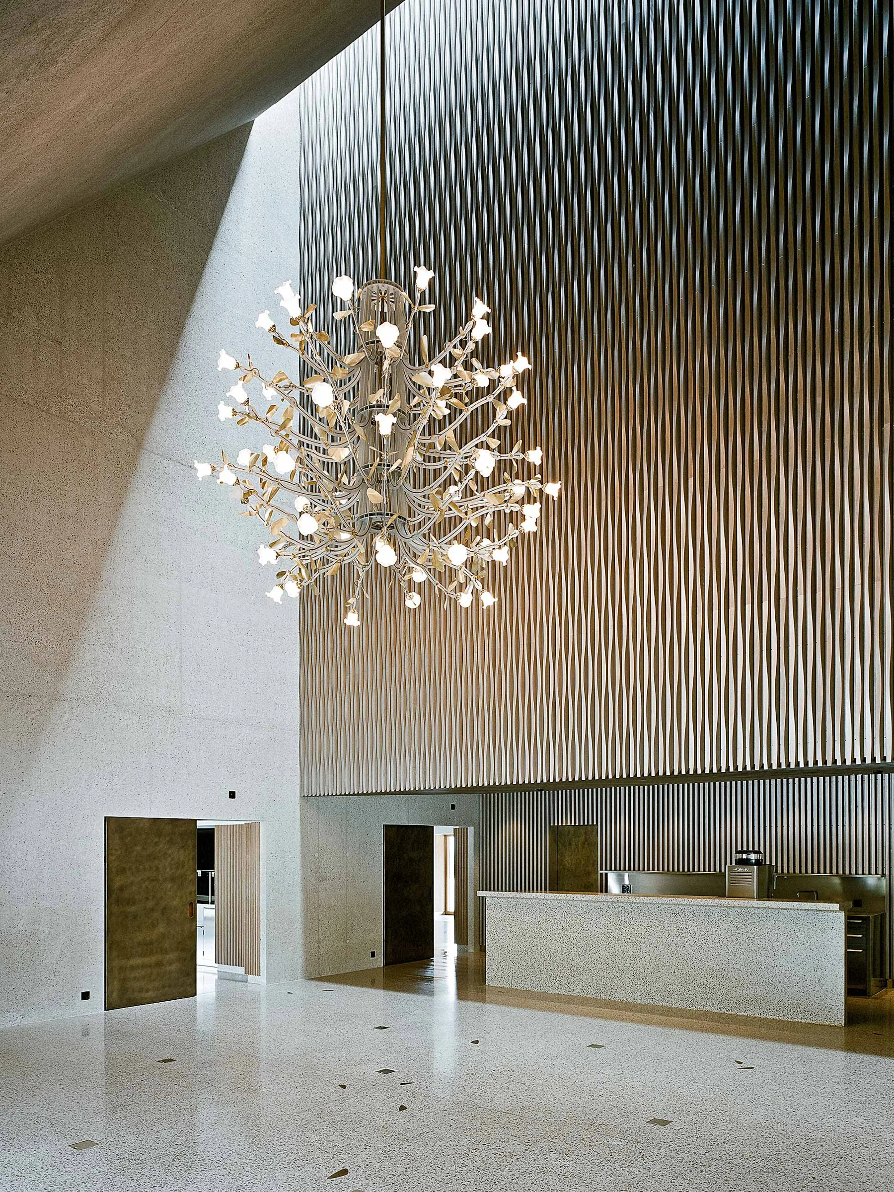 High foyer with a textured metal wall, a large branching chandelier and a stone floor