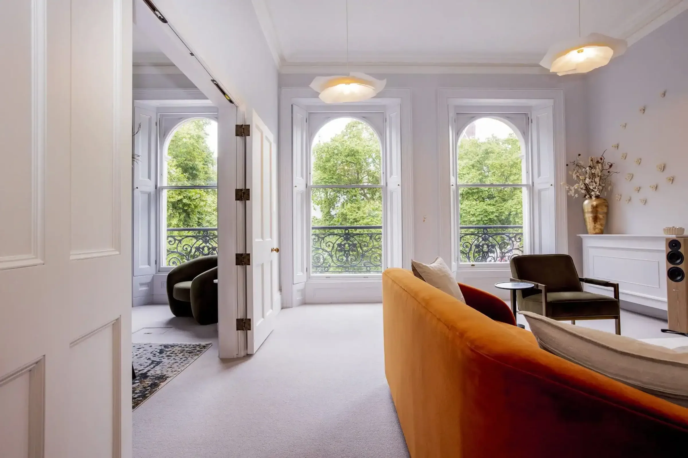 View through an open white door into a lounge with an orange sofa and arched windows onto trees