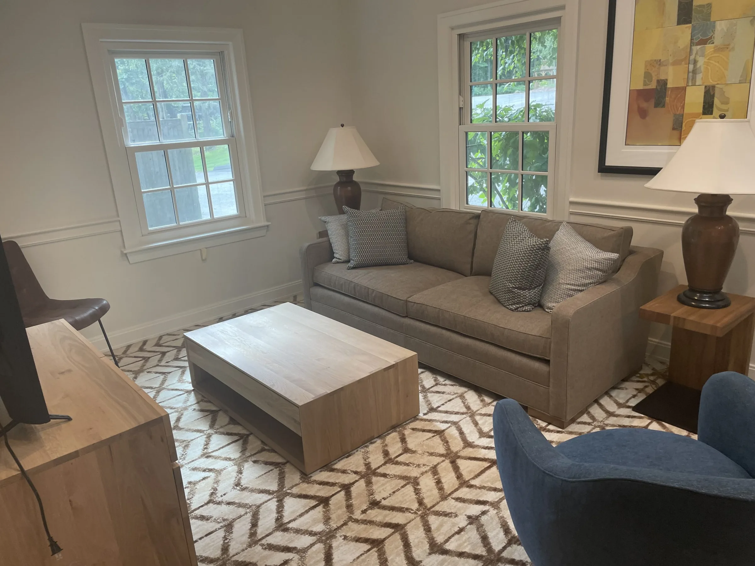 Sitting room with a grey sofa, wooden coffee table, patterned rug and two sash windows