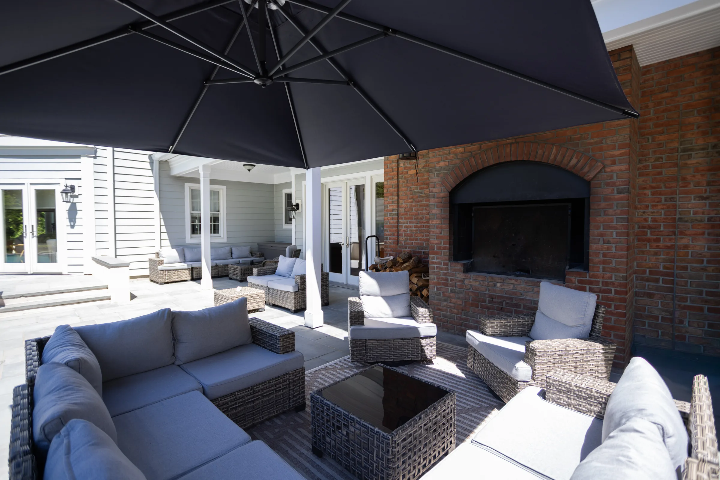 Covered patio with grey wicker sofas, a brick outdoor fireplace and a large black parasol